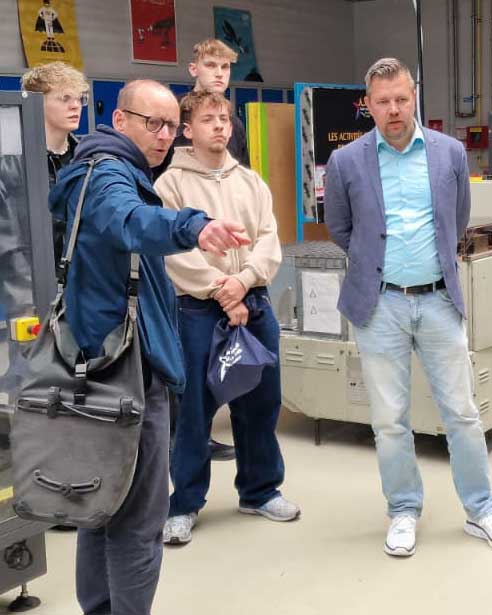 Ein französischer Lehrer deutet auf etwas, das im Bild nicht zu sehen ist, und erklärt den deutschen Besuchern etwas dazu.