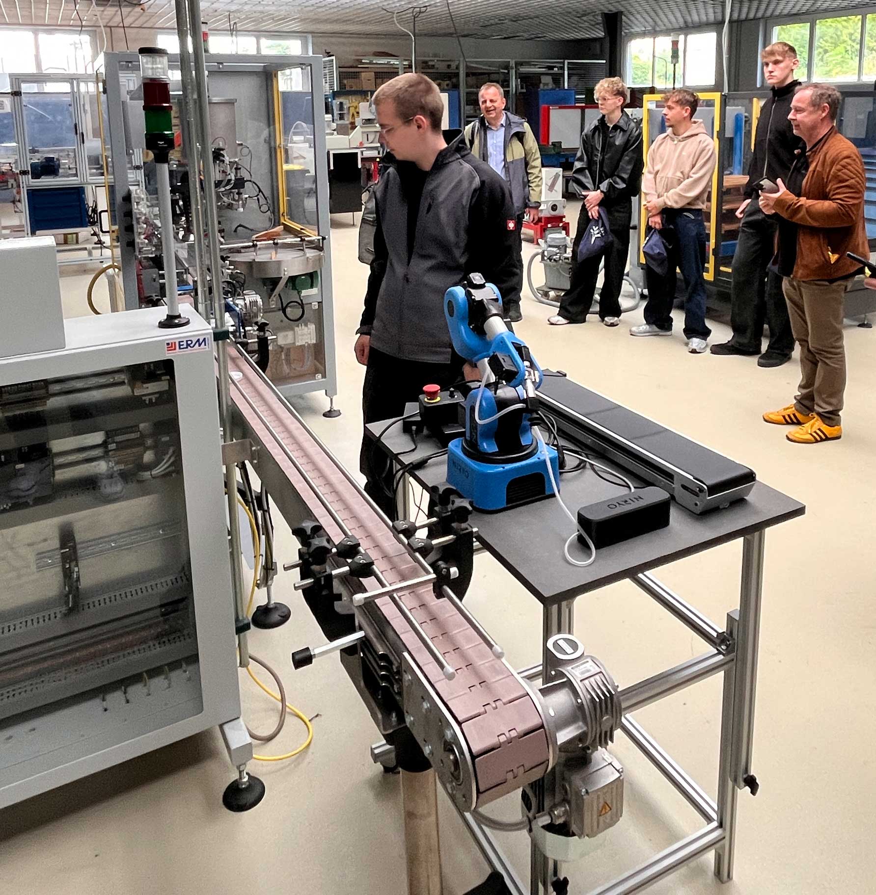 Ein deutscher Azubi schaut sich eine Maschine in der französischen Schule aus nächster Nähe an. Weitere Azubis und Betreuer schauen aus etwas Abstand zu.