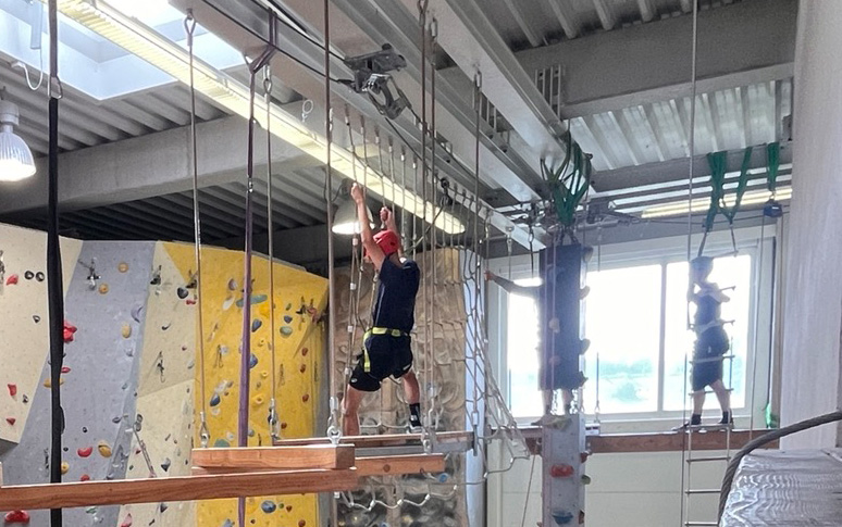 Drei Auszubildende balancieren in der Kletterhalle über ein Kletterelement.