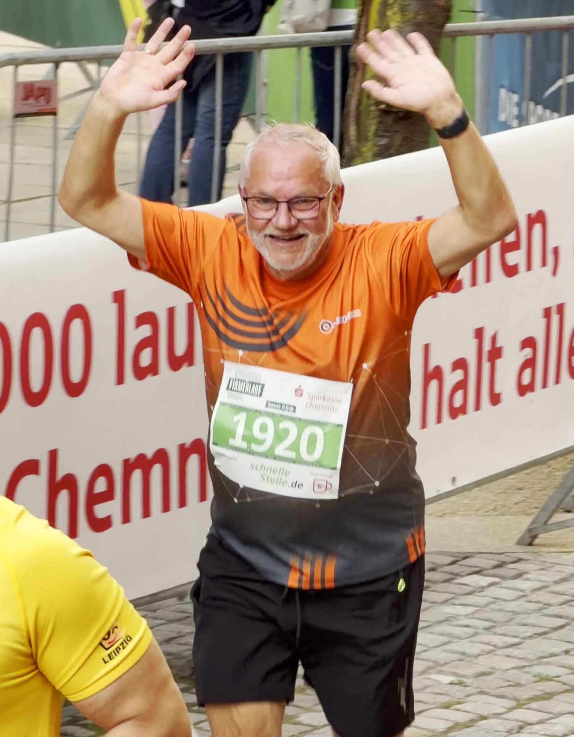 Ein Mitarbeiter von Sachsen Guss läuft beim Firmenlauf Chemnitz 2026. Er reckt beide Arme in die Höhe und winkt.