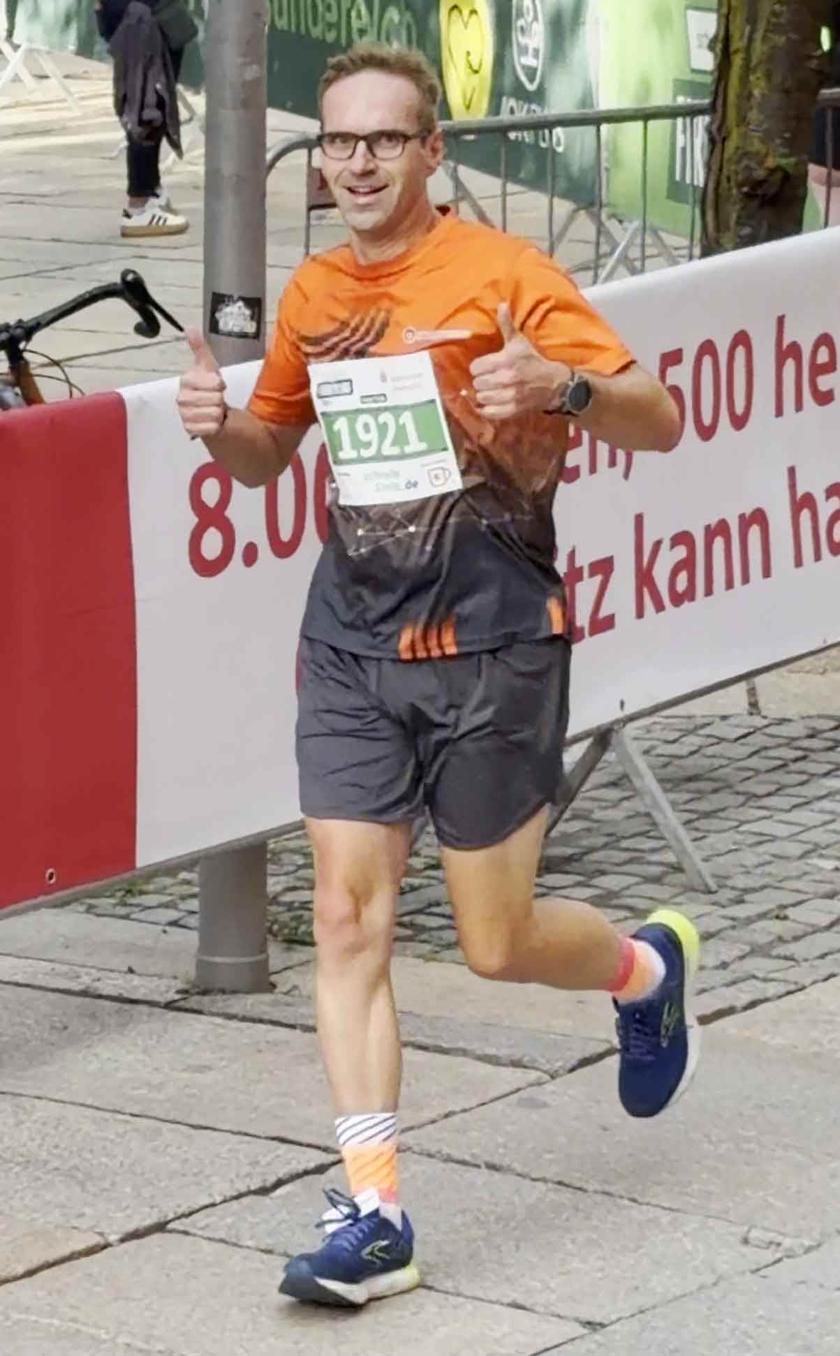 Ein Mitarbeiter von Sachsen Guss läuft beim Firmenlauf Chemnitz 2026. Er hat die Hände zu Fäusten geballt und reckt beide Daumen in die Höhe.