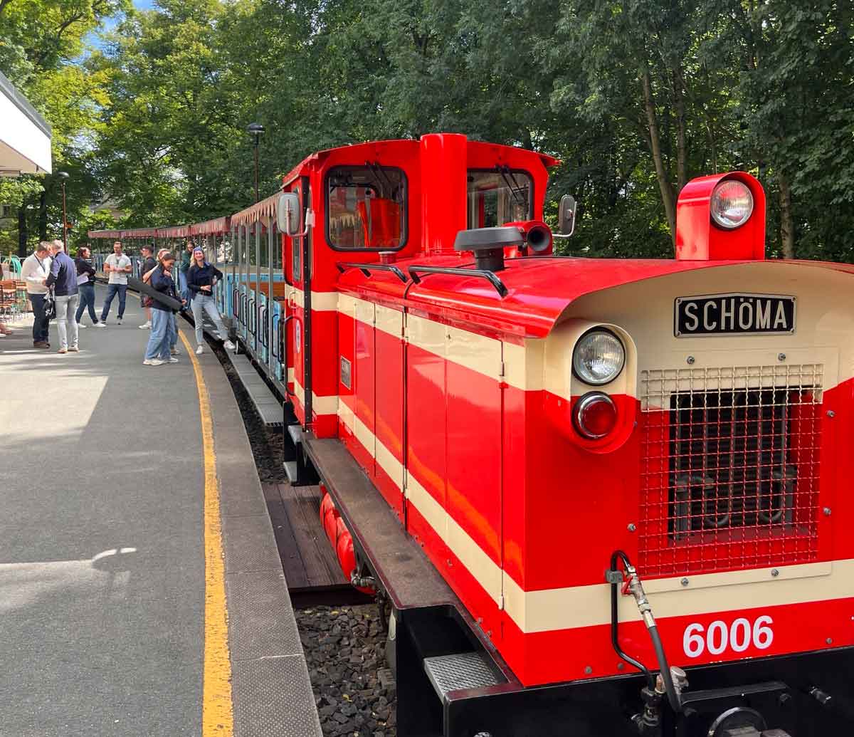 Die Parkeisenbahn Chemnitz steht an einem Bahnsteig. Auf dem Bahnsteig stehen mehrere Menschen.