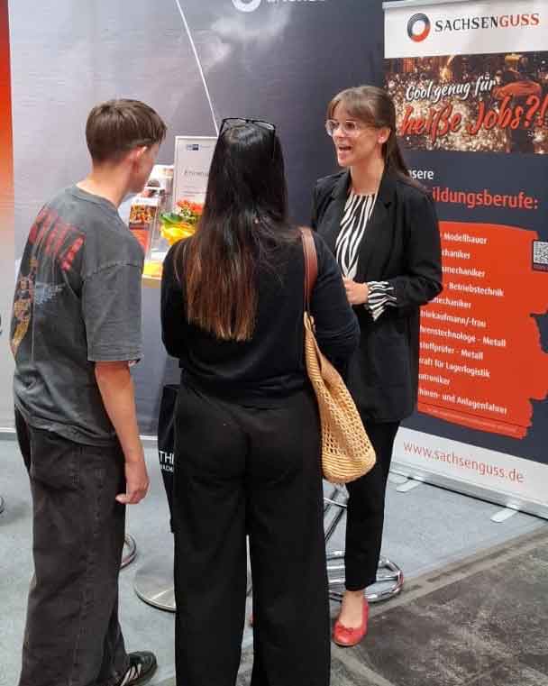 Eine Mitarbeiterin von Sachsen Guss spricht auf der Messe mach was! mit einer Frau und einem Jugendlichen.