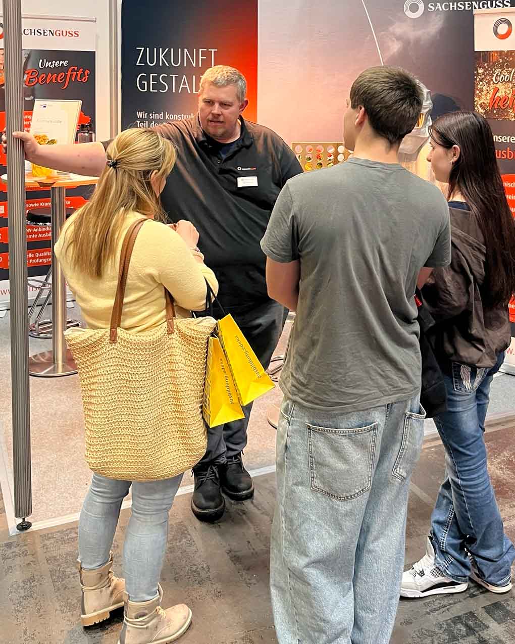 Ein Mitarbeiter von Sachsen Guss spricht auf der Messe mach was! mit einer Frau sowie einem jungen Mann und einer jungen Frau.